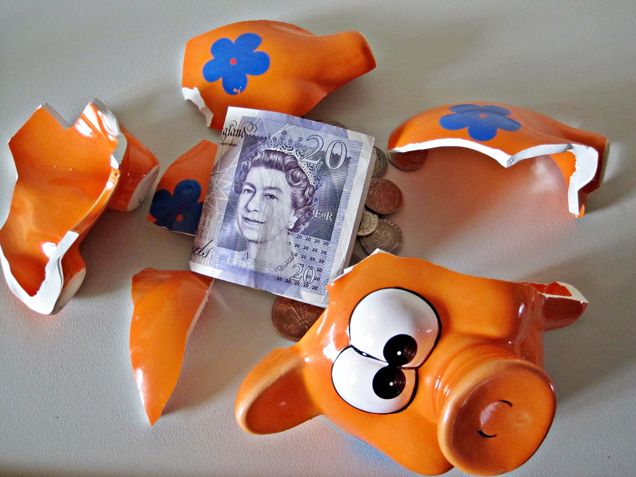 A smashed piggy bank with a UK £20 note and some coins inside