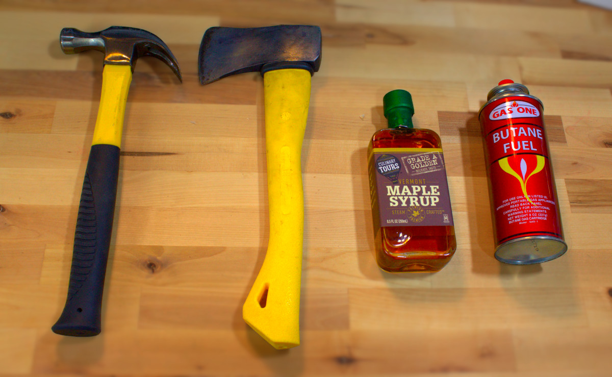 A series of decreasingly hammer-like objects: A hammer, an axe, a bottle of maple syrup and a can of butane fuel.
